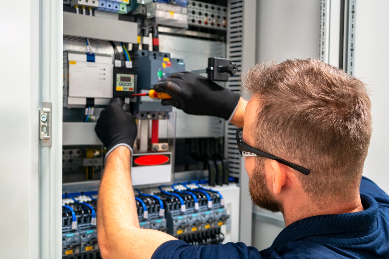 Ein Elektroniker mit Schutzbrille und Handschuhen arbeitet an einem Schaltschrank