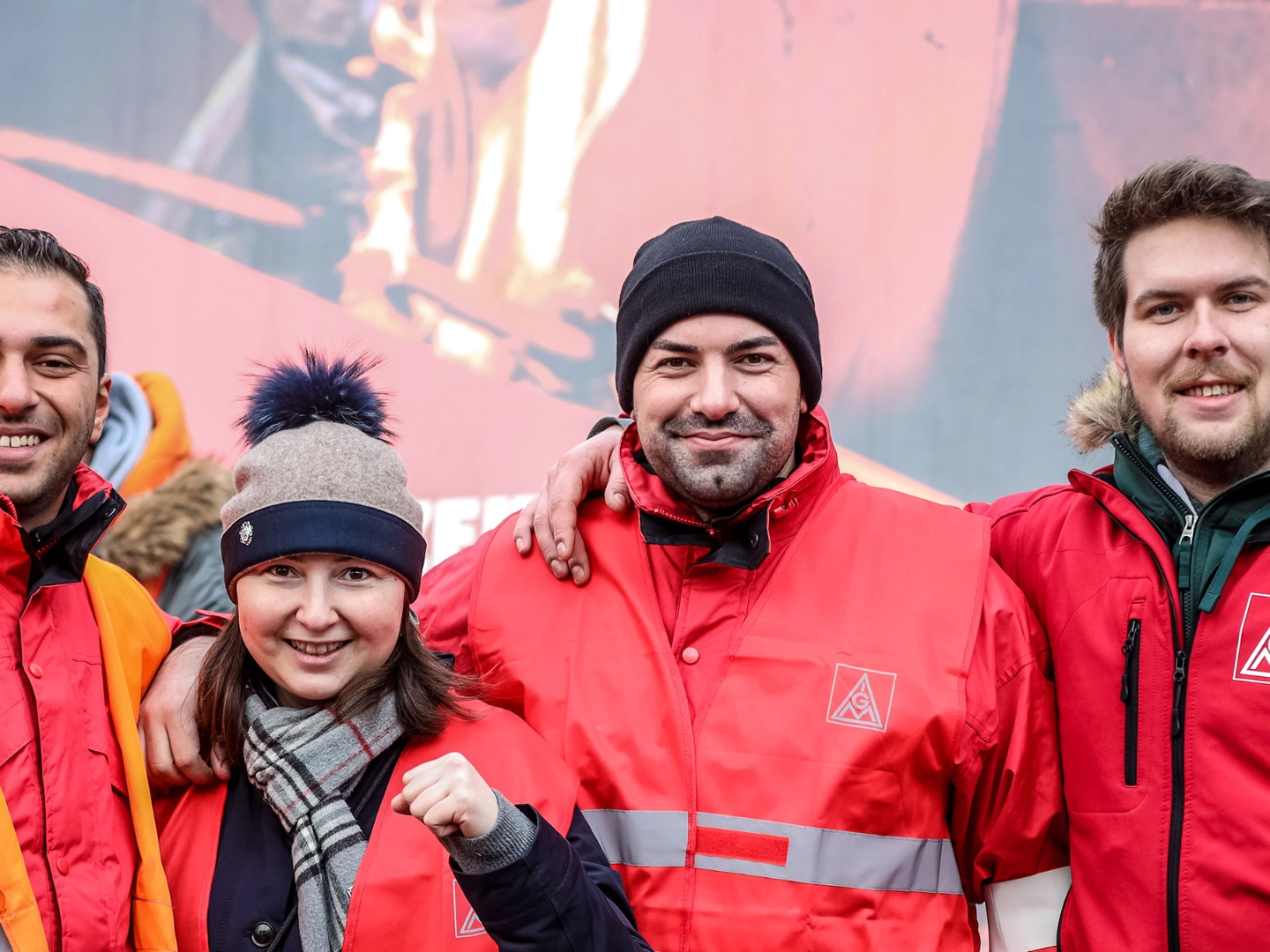 Eine Frau und drei Männer ballen die Fäuste und lächeln in die Kamera.