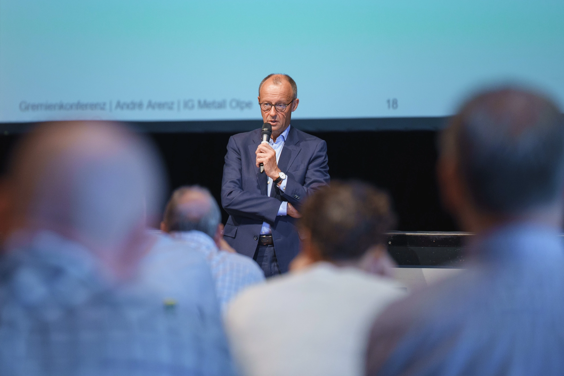 Friedrich Merz spricht vor Gremienkonferenz der IG Metall Olpe. Er spricht in ein Mikrofon vor den Teilnehmenden welche verschwommen im Vordergrund des Bildes sichtbar sind.