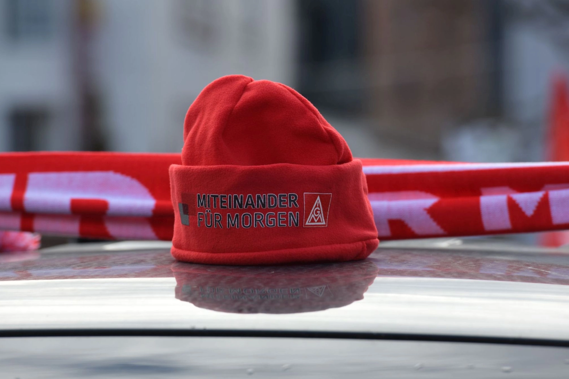 Rote IG Metall-Mütze mit Schriftzug "Miteinander für morgen" auf Autodach
