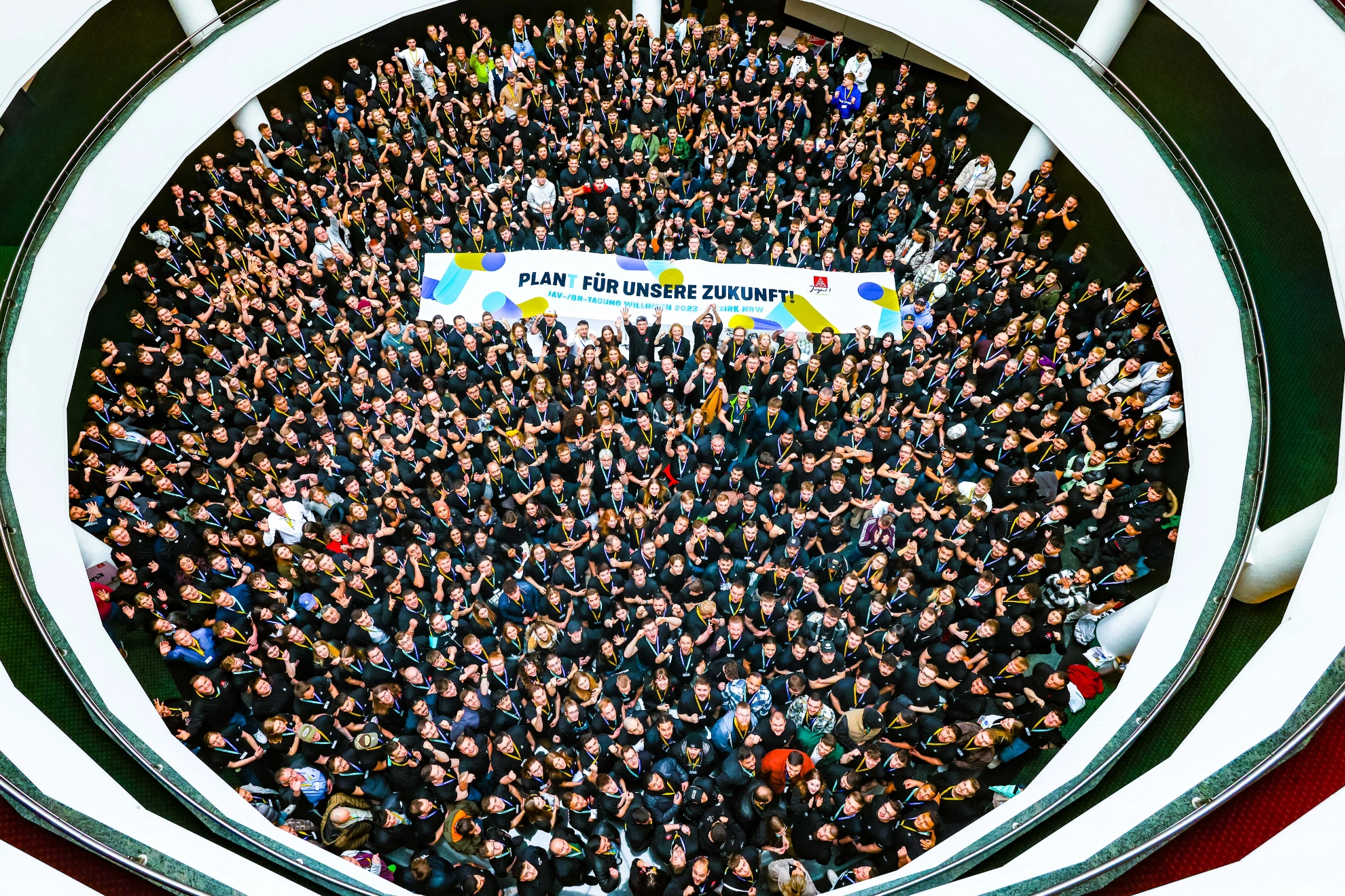 1000 Teilnehmende aus Nordrheinwestfalen im Lichthof des Sauerlandsterns in Willingen schauen nach oben in die Kamera und halten ein Banner mit der Aufschrift Plant für unsere Zukunft.