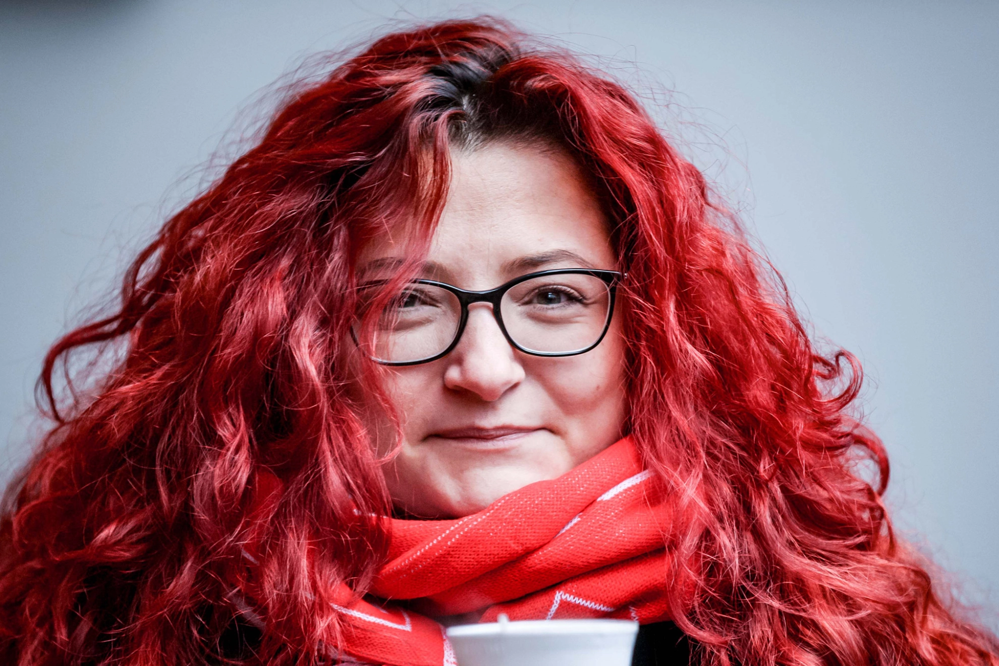 Eine Frau mit roten Locken hält einen Kaffeebecher.