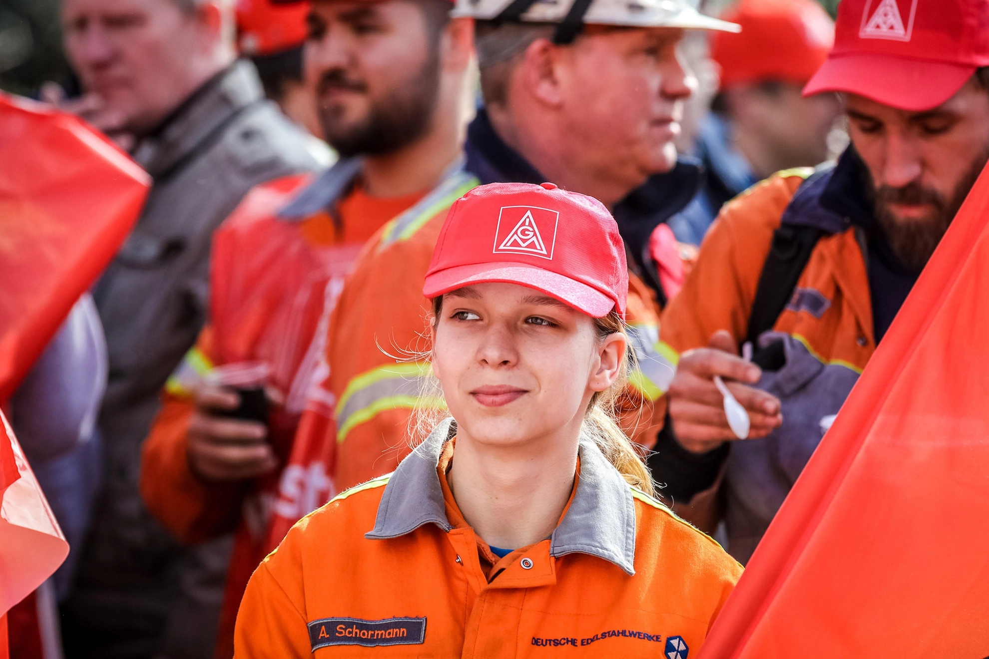 Eine junge Frau mit IG Metall-Kappe, einer Fahne und Arbeitskleidung auf einer Demo.