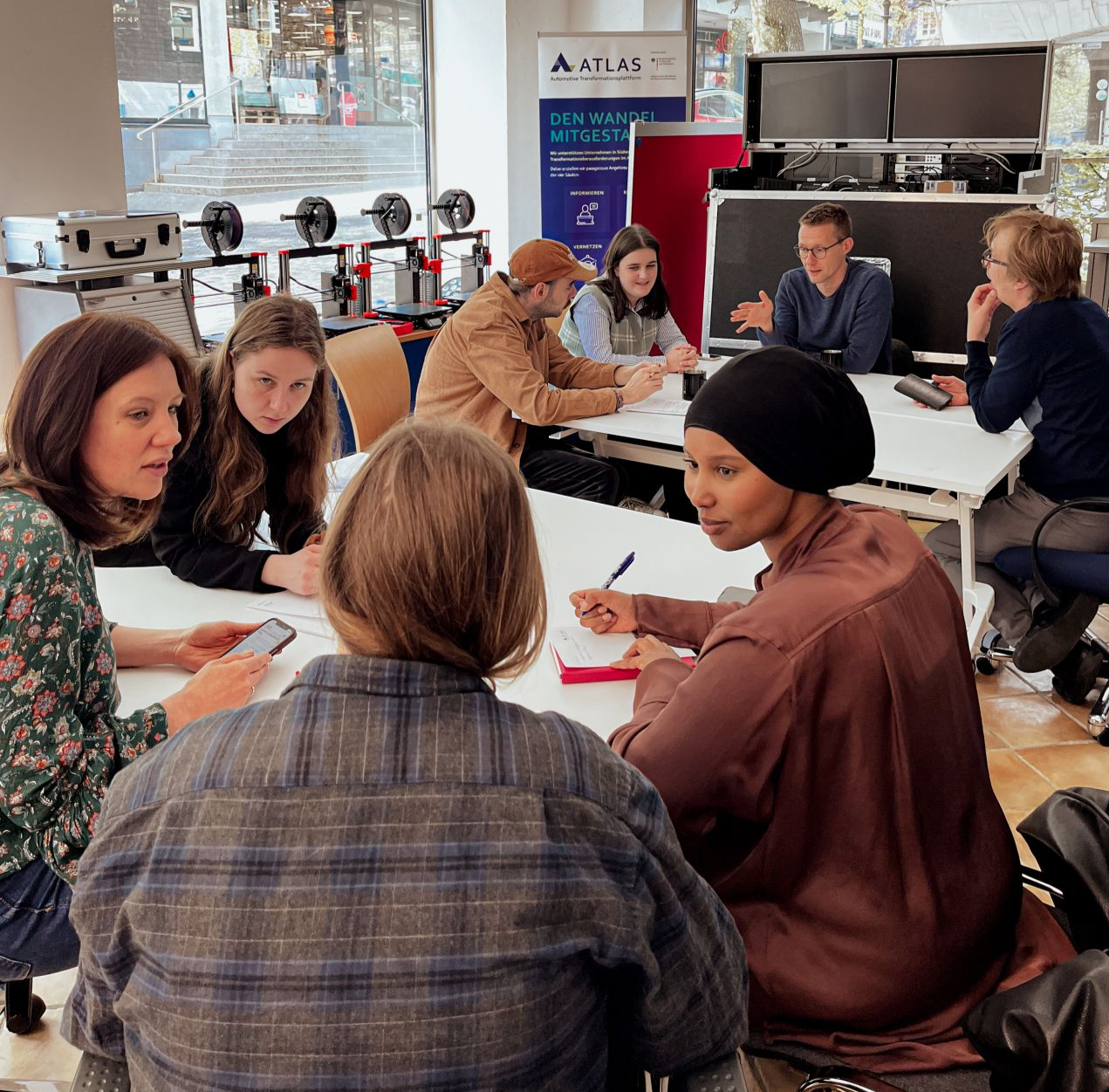 Eine Gruppe Teilnehmende spricht über Möglichkeiten und Projekte im Innovationslabor Olpe. Menschen sitzen an Gruppentischen und unterhalten sich.