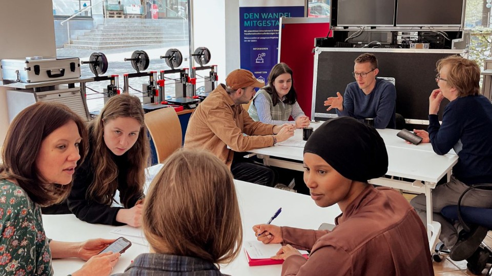 Eine Gruppe Teilnehmende spricht über Möglichkeiten und Projekte im Innovationslabor Olpe. Menschen sitzen an Gruppentischen und unterhalten sich.